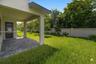 Covered patio with paver flooring, expansive lawn, and concrete privacy wall