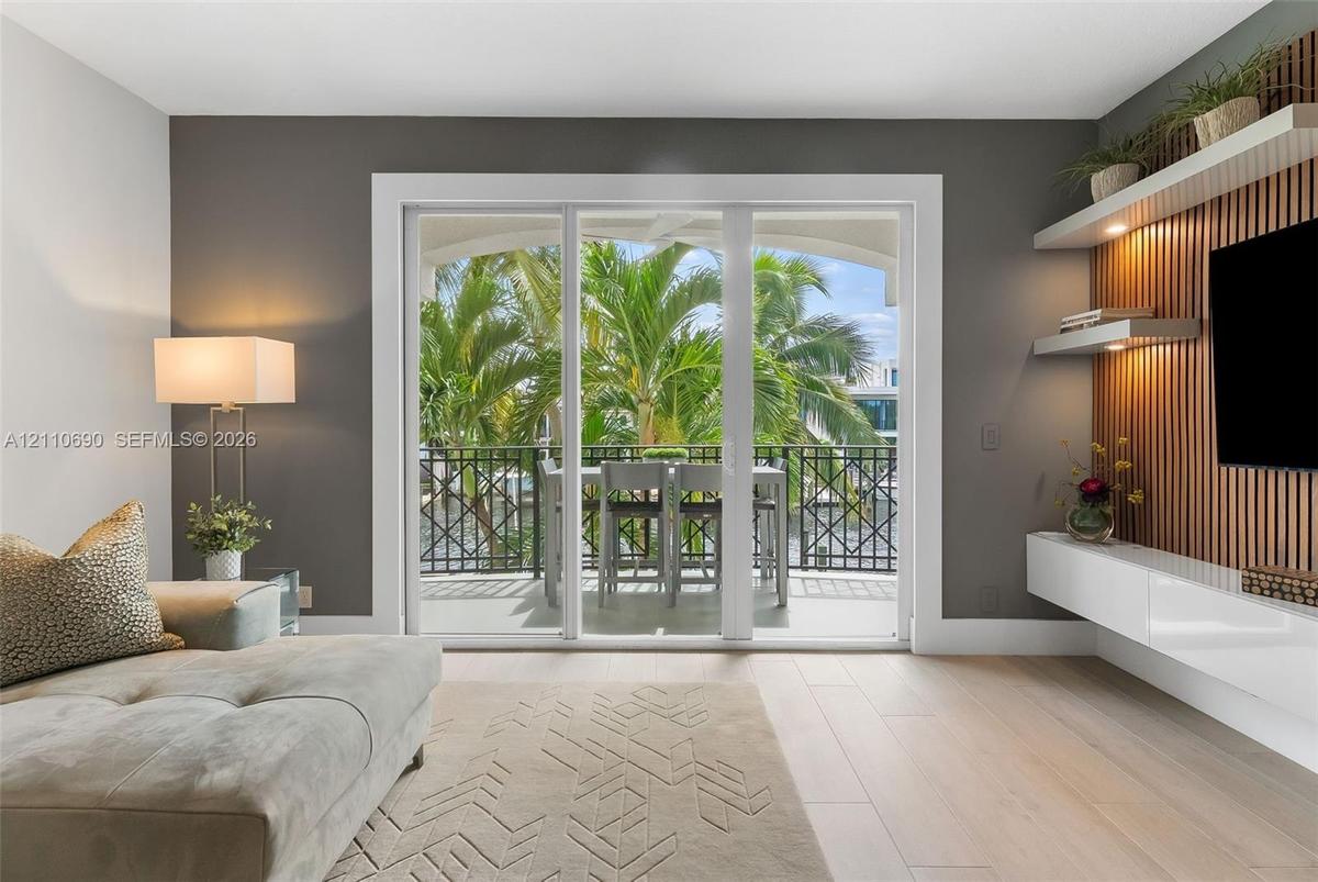 Sliding glass doors opening to a covered balcony with decorative metal railing, wood-slat accent wall with integrated shelving, and white high-gloss f