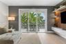 Sliding glass doors opening to a covered balcony with decorative metal railing, wood-slat accent wall with integrated shelving, and white high-gloss f