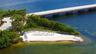 Private waterfront sandy beach featuring a perimeter fence, mature landscaping, and stone bulkhead
