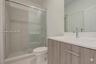 Bathroom featuring a vanity with a light wood-finish cabinet and an integrated countertop, a glass-enclosed shower with tiled surround, and a wall-mou