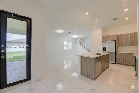 Open-concept interior featuring light-toned stone-finish flooring, recessed lighting, and a kitchen equipped with wood-finish cabinetry, a quartz-topp