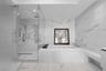 Large-format white tile with grey veining, glass-enclosed walk-in shower with rainfall showerhead, and a deep-soaking drop-in bathtub