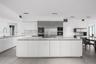 Contemporary kitchen featuring an expansive center island with stone surfacing, stainless steel built-in appliances, flat-panel cabinetry, a stone bac