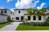 Two-story exterior featuring light-toned smooth stucco finish, horizontal siding accents, dark-framed windows, paver driveway, and professional landsc