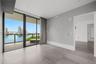 Floor-to-ceiling sliding glass doors, large-format grey tile flooring, recessed ceiling lighting, and a private balcony featuring a glass railing