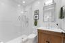 Bathroom featuring a walk-in shower with frameless glass enclosure, handheld shower fixture, wood-finish vanity with countertop sink, and wall-mounted