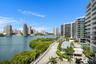 High-rise architecture with expansive glass-railed balconies, waterfront location, multi-level swimming pools, and landscaped grounds with mature palm