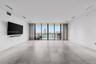 Large-format tile flooring, recessed linear lighting, and expansive floor-to-ceiling glass paneling leading to a balcony with water and skyline scener