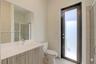 Bathroom featuring a vanity with a light wood-finish cabinet and solid surface countertop, an oversized wall-mounted mirror, a full-height glass-panel