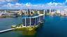 Waterfront high-rise building situated on a private peninsula, featuring wraparound balconies, an outdoor swimming pool, lush landscaping, and direct 