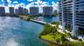 High-rise residential exterior featuring stacked private balconies, waterfront grounds with palm trees, and direct access to a private dock facility