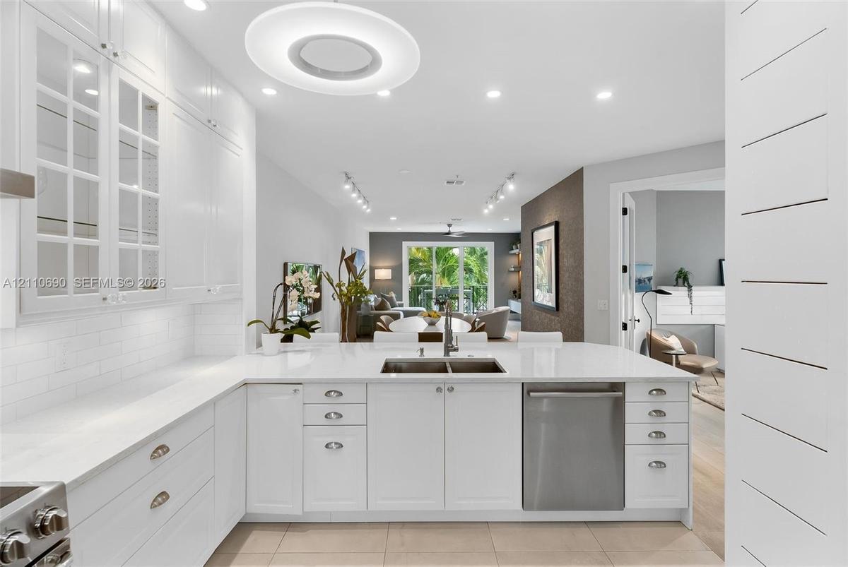 White cabinetry featuring glass-paneled upper doors, expansive countertops with an integrated stainless steel dual-basin sink, stainless steel dishwas