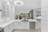 White cabinetry featuring glass-paneled upper doors, expansive countertops with an integrated stainless steel dual-basin sink, stainless steel dishwas