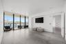 Large-format tile flooring, floor-to-ceiling glass paneling, and an attached balcony with metal railing overlooking the waterfront and cityscape