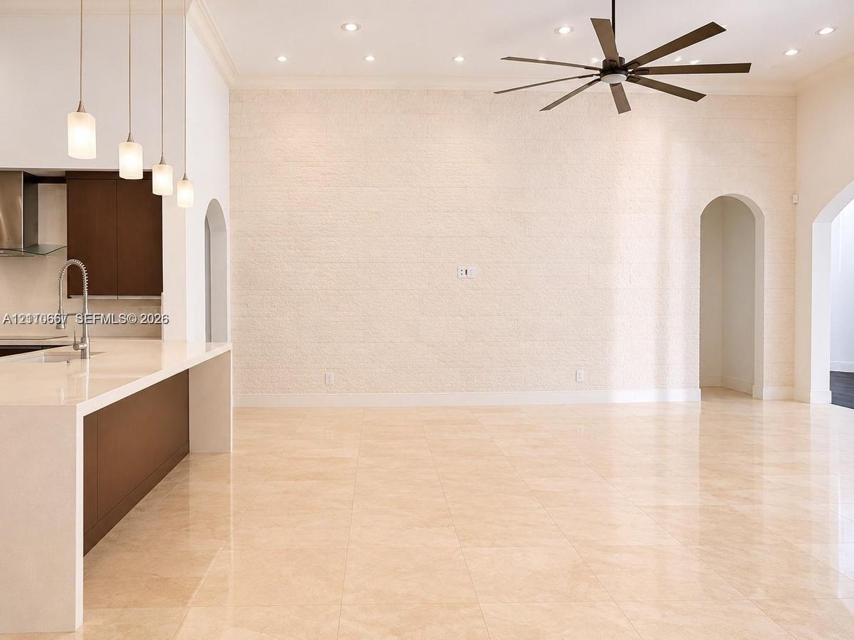 Open-concept interior featuring a textured stone accent wall, polished tile flooring, recessed lighting, four modern pendant lights, and a high ceilin