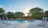Free-form swimming pool featuring a waterfall feature and stone masonry retaining walls, surrounded by a light-toned paver deck and mature landscaping