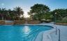 Swimming pool featuring a rock-faced water feature, paver-stone decking, metal handrails, and surrounding mature landscaping