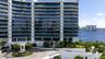 Mid-rise architectural exterior featuring tiered glass balconies, floor-to-ceiling windows, white structural columns, a circular paved motor court, an