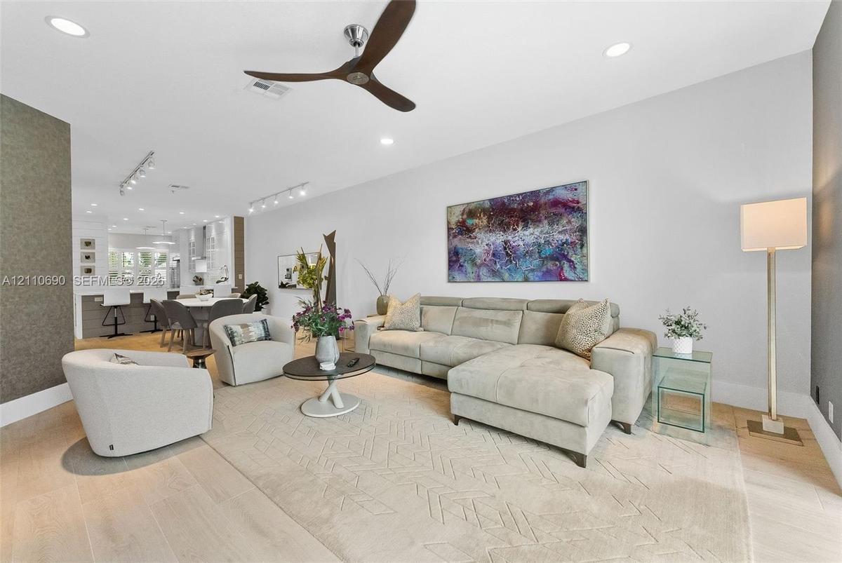 Open-concept interior featuring light-toned wood-finish flooring, recessed lighting, track lighting, and a contemporary three-blade ceiling fan