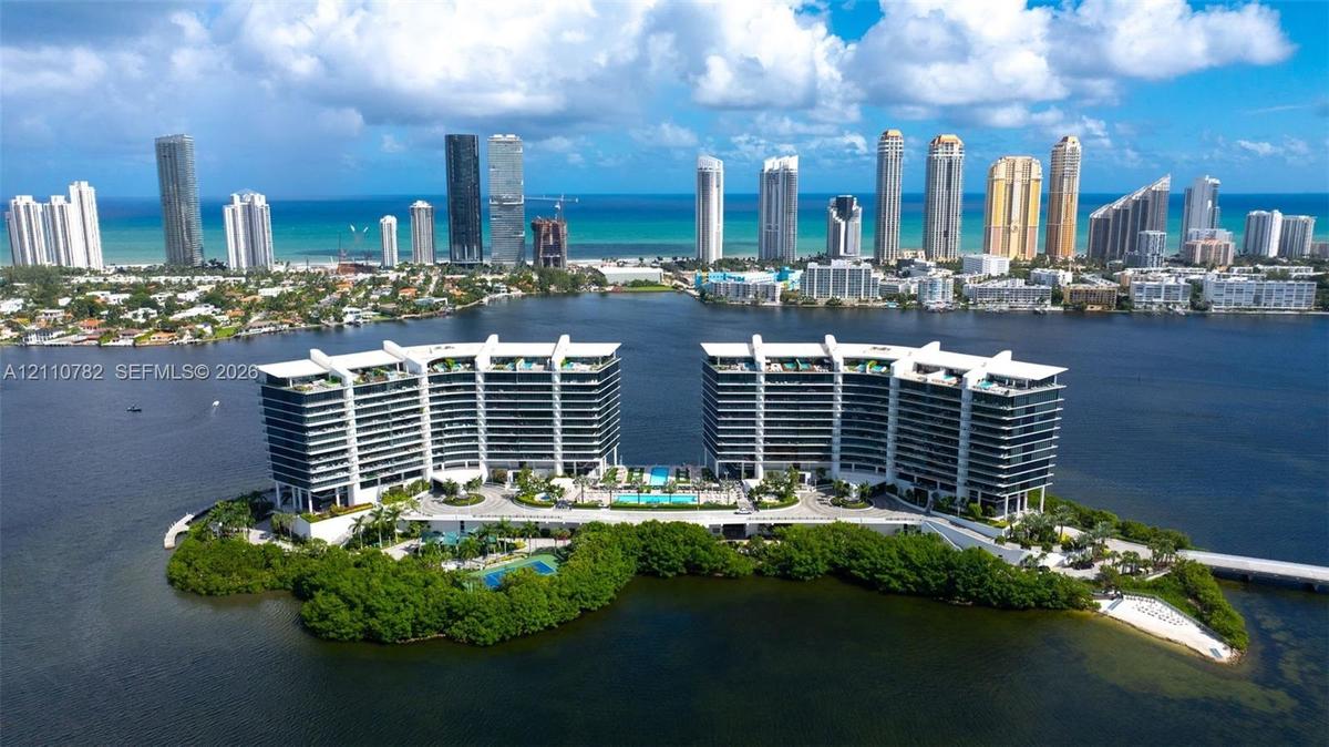 Waterfront high-rise complex situated on a private island, featuring tiered architectural profiles, expansive glass balcony systems, a central outdoor