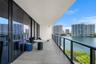 Covered balcony featuring large-format stone-finish tiling, full-height glass sliding doors, and a sleek metal railing with glass panels