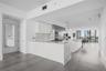 Kitchen featuring a stone-finish island with waterfall edge, white flat-panel cabinetry, stainless steel built-in appliances, and large-format floor t