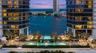 Waterfront high-rise complex featuring dual glass-facade towers, multiple swimming pools, professional landscaping, and paved outdoor terrace space