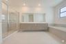 Floating vanity with double under-mount sinks, expansive wall-to-wall mirror, glass-enclosed walk-in shower, built-in soaking tub with stone surround,