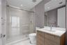 Bathroom featuring a glass-enclosed walk-in shower with tile surround, vanity with a light-tone wood finish, solid-surface countertop, and an integrat
