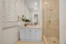 Bathroom featuring white cabinetry, stone-surface countertop, undermount sink, brass-finish fixtures, and a glass-enclosed shower with floor-to-ceilin