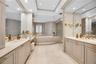 Dual vanities with recessed-panel cabinetry, stone countertops, integrated basins, recessed lighting, and a raised platform soaking tub