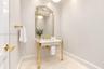 Console-style sink with stone countertop, polished gold-tone metal legs, decorative framed mirror, and coordinating gold-tone faucet and hardware