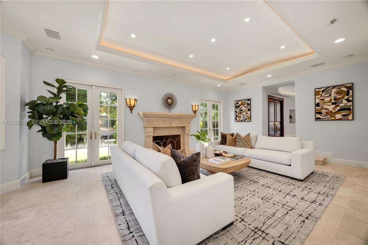 Tray ceiling with recessed lighting, carved stone fireplace surround, tile flooring, and dual sets of French doors with glass panes
