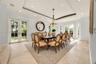Formal dining area featuring tray ceilings with recessed lighting, stone flooring, a multi-light chandelier, and dual sets of glass-paneled French doo