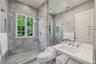 Full-wall natural stone tiling, glass-enclosed shower, wall-to-wall vanity mirror, porcelain sink with polished chrome widespread faucet, and multi-pa