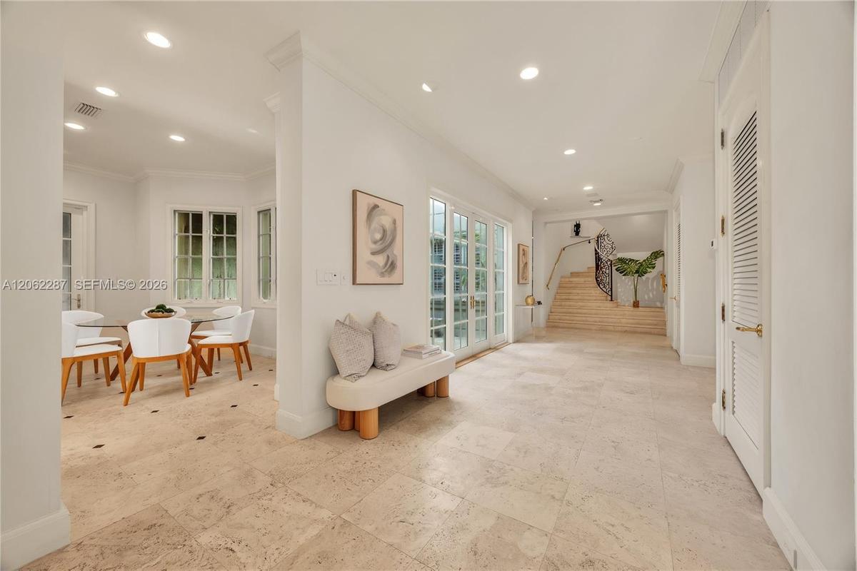 Open interior featuring large-format stone tile flooring, recessed lighting, double-paned glass French doors, and a staircase with a wrought-iron rail