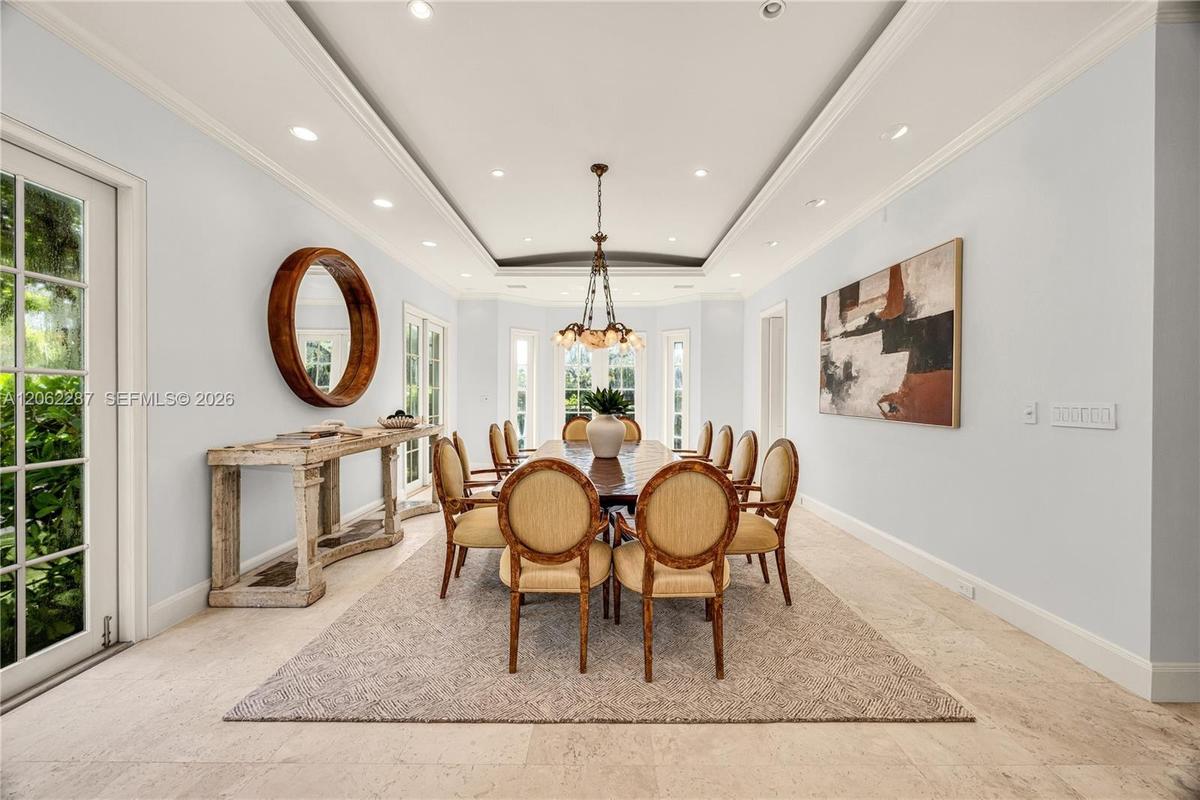 Tray ceiling with recessed lighting, stone flooring, multiple glass-paneled exterior doors, and a multi-arm chandelier