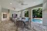 Covered outdoor loggia featuring stone paver flooring, architectural columns with arched openings, recessed lighting, and ceiling fans, overlooking a 