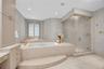 Raised stone-surround soaking tub with gold-tone fixtures, walk-in glass-enclosed shower, custom built-in cabinetry, floor-to-ceiling stone wall cladd