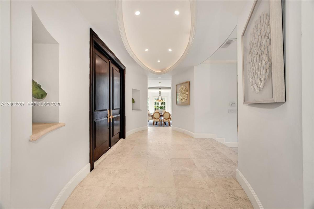 Foyer featuring stone tile flooring, double-door entry with brass hardware, oval tray ceiling with recessed lighting, and integrated wall niches