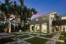Covered loggia featuring arched architectural details, integrated swimming pool, structured paver and turf patio, and mature tropical landscaping