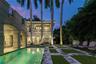 Exterior space featuring a rectangular swimming pool, stone-paver hardscaping, grid-patterned turf landscaping, mature palm trees, and two-story struc