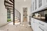 Spiral staircase with metal railing and wood-finish treads, custom white cabinetry featuring glass-front upper doors, dark stone-finish countertops, s