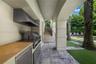 Covered outdoor kitchen featuring a built-in stainless steel grill, range hood, and solid surface countertop, complemented by stone tile flooring, arc