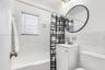 Bathroom featuring a white vanity cabinet, square wall tile surround, circular mirror with a black frame, and a tub-shower combination