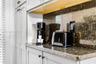 Custom cabinetry with matte black hardware, stone-finish countertops, coordinating backsplash, and open wood shelving