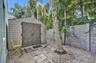 Exterior storage shed featuring dual-panel doors, accompanied by a stone-pattern privacy wall, stone paver pathway, and gravel ground cover