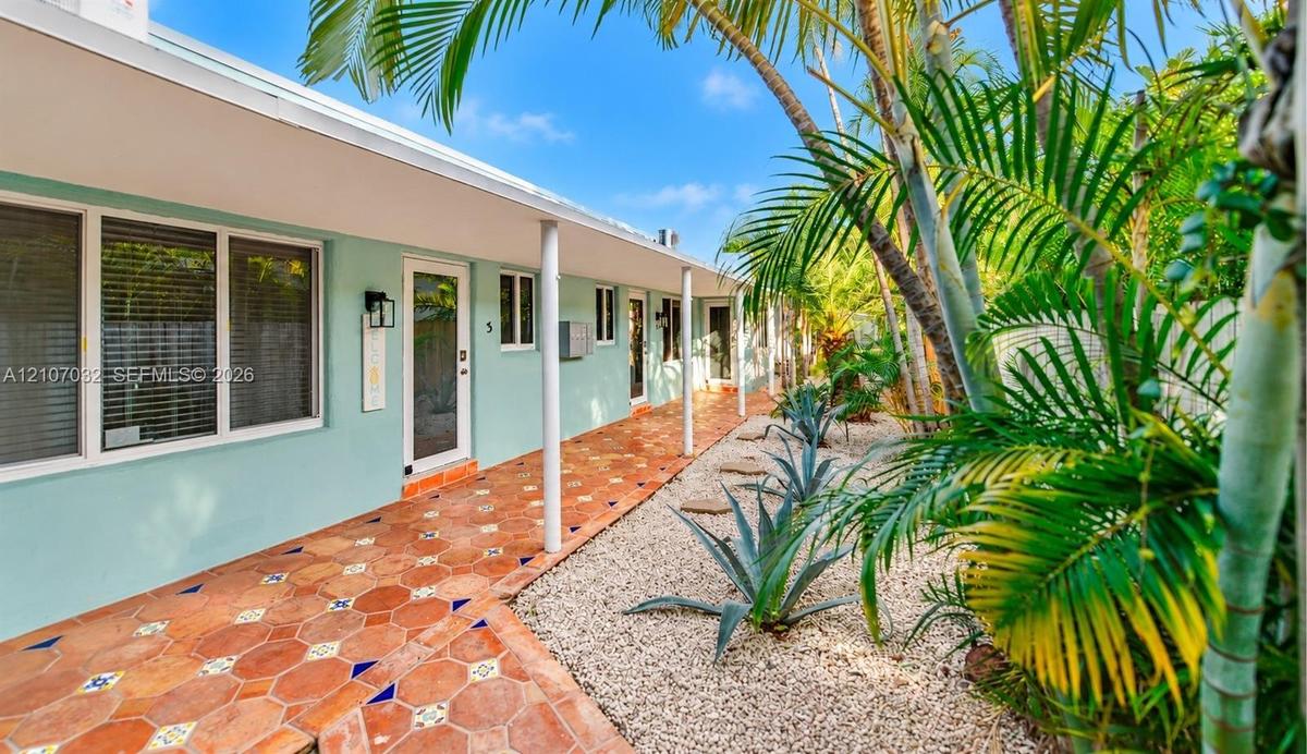Exterior walkway featuring terracotta tile flooring with decorative inserts, covered porch supported by structural columns, and xeriscaped garden beds