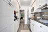 Galley kitchen featuring white shaker-style cabinetry, stone countertops, integrated stainless steel appliances, dark stone backsplash, and wood-finis